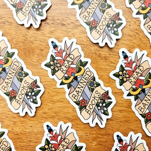 May include: A set of nine stickers featuring a stylised dagger with a banner reading "Read Banned Books". The dagger is decorated with flowers and the banner is in a vintage style.