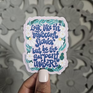 May include: A sticker with a pink background and white flowers. The text on the sticker reads "Look like the innocent flower but be the serpent under it".