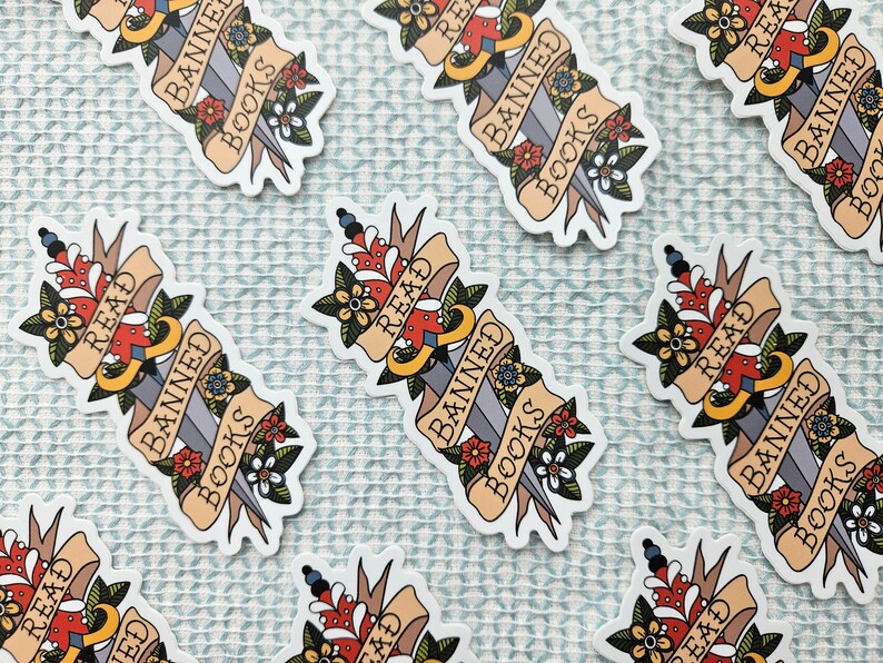 May include: A set of six stickers featuring a stylised dagger piercing through a banner that reads "Read Banned Books". The dagger is decorated with flowers and the banner is in a vintage style.