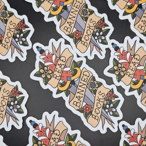 May include: A set of colourful stickers featuring a dagger and the words "Banned Books, Read" on a banner. The stickers are designed to look like traditional tattoo flash art.