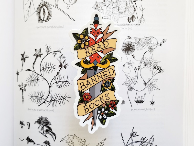 May include: A sticker featuring a dagger and a banner that reads "Read Banned Books". The dagger is adorned with red, yellow, and blue flowers. The banner is yellow with red and blue accents.