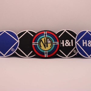May include: Five round embroidered patches with white stitching. The patches are blue, black, and red with white and yellow accents. The patches feature the text "H&I" and "NA".