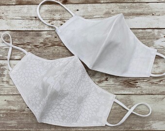 May include: Two white face masks, one with a floral pattern and the other plain. Both masks have elastic ear loops.