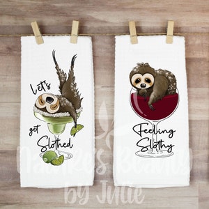 May include: Two white kitchen towels with sloth illustrations and text. The first towel features a sloth hanging from a margarita glass with the text "Let's get Slothed". The second towel features a sloth in a glass of red wine with the text "Feeling Slothy".