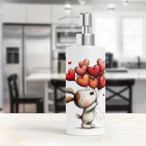 May include: White ceramic soap dispenser with a silver pump. The dispenser features a cartoon dog holding a bouquet of heart-shaped balloons in shades of red and orange. Small red hearts are scattered around the design.