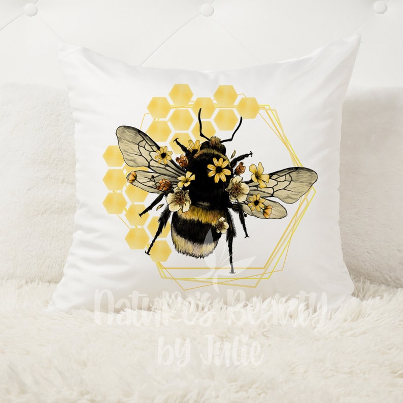 May include: A white throw pillow with a yellow and black bumblebee surrounded by yellow flowers and a honeycomb pattern. The bee is in a gold geometric frame.