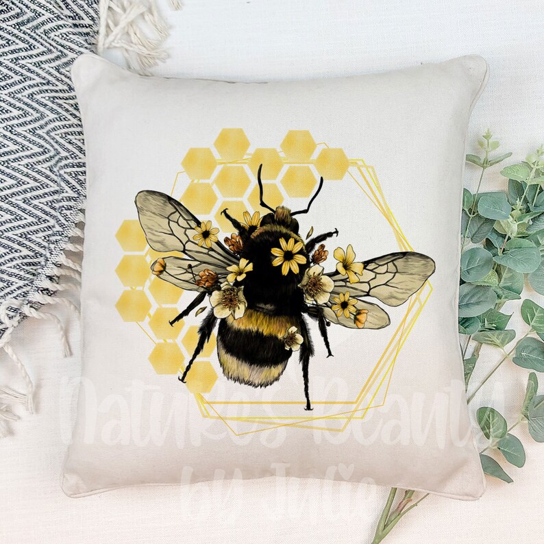 May include: A beige throw pillow with a yellow and black bumblebee illustration. The bumblebee is surrounded by yellow flowers and a honeycomb pattern. The honeycomb pattern is outlined in gold.