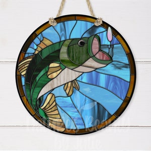 May include: A stained glass window hanging ornament featuring a green and white bass fish jumping out of the water with a fishing lure in its mouth. The background is blue with brown and yellow accents.