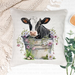 May include: A black and white cow peeking out of a metal bucket filled with pink and white flowers. The cow is surrounded by green leaves and the bucket is sitting on a white background.