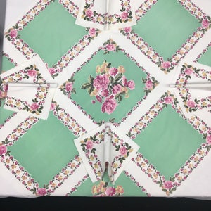 Op de afbeelding: Een wit tafelkleed met een groen en bloemig patroon. Het tafelkleed heeft een ruitpatroon met een bloemig ontwerp in het midden van elke ruit. Het tafelkleed is versierd met roze en gele bloemen.
