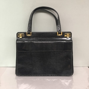 May include: A black leather handbag with a textured snakeskin pattern and gold hardware. The bag has a top handle and a flap closure.