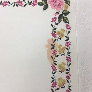 Op de afbeelding: Witte tafelkleed met een roze en gele bloemenrand. Het tafelkleed heeft een vlek in het midden.