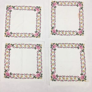 Op de afbeelding: Vier witte servetten met een roze en gele bloemenrand. De servetten zijn gevouwen en in een vierkant patroon gerangschikt.