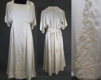 May include: A white satin dress with a matching jacket. The dress has a simple design with a scoop neck and short sleeves. The skirt is full and flowing. The dress is decorated with delicate beading around the hemline.