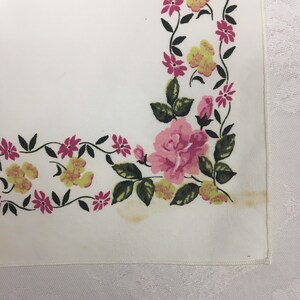 Op de afbeelding: Witte stof met een bloemenpatroon van roze en gele bloemen met groene bladeren. Het patroon bevindt zich rond de rand van de stof.
