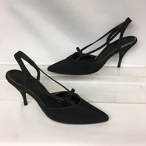 May include: A pair of black satin high-heeled shoes with a slingback strap and a bow detail on the front.