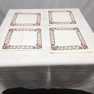 Op de afbeelding: Set van vier witte placemats met een roze en gele bloemenrand.