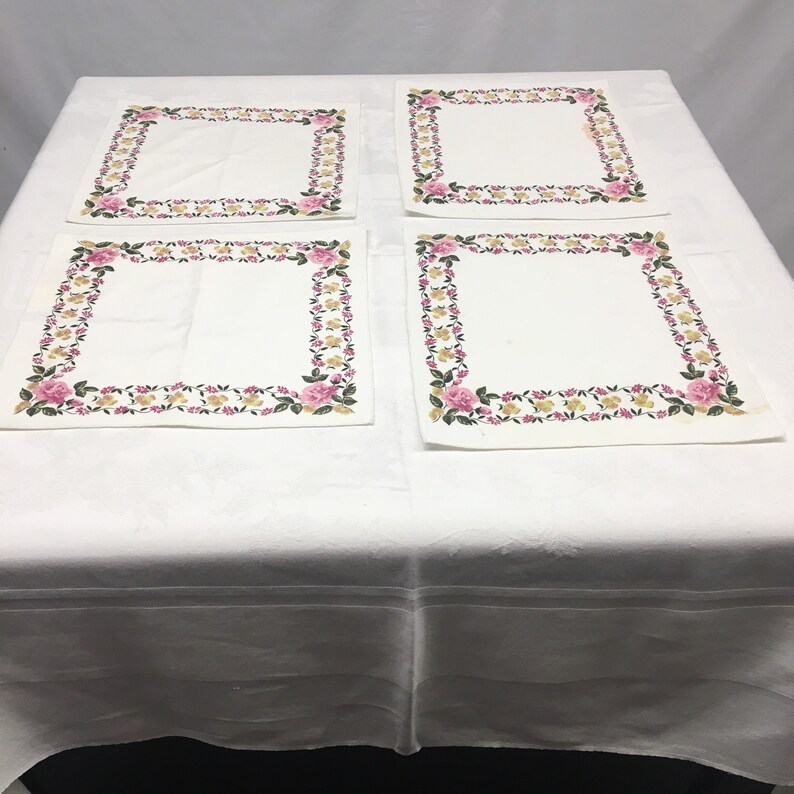 Op de afbeelding: Set van vier witte placemats met een roze en gele bloemenrand.