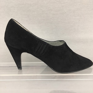 May include: Black suede heeled shoes with a pointed toe and a unique angled heel.