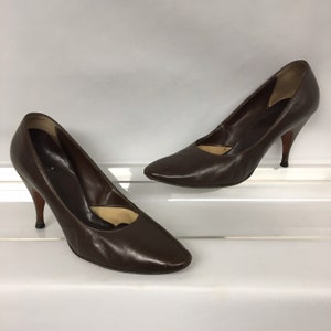 May include: A pair of brown leather pumps with pointed toes and stiletto heels. The shoes have a classic design, with a smooth, polished finish. The heels are approximately 3 inches (7.6 cm) high.