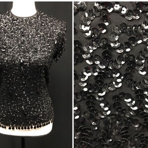 May include: A black sequined top with short sleeves and a round neckline. The top has a fringe trim at the bottom.
