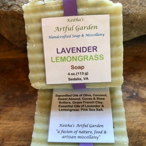 May include: Two bars of handcrafted Lavender Lemongrass soap from Keitha's Artful Garden, held together with a purple ribbon. The soap is light green with visible herbs and includes the ingredients: olive oil, coconut, sweet almond, cocoa & shea butters, and pink sea salt.
