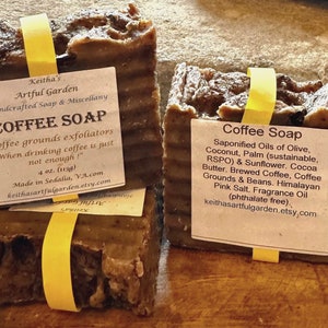 Peut inclure: Deux savons au café bruns avec des étiquettes indiquant "Coffee Soap". L'étiquette du haut indique "Coffee grounds exfoliators "When drinking coffee is just not enough!" 4 oz. (113g) Made in Sedalia, VA.com keithasartfulgarden.etsy.com". L'étiquette du bas indique "Saponified Oils of Olive, Coconut, Palm (sustainable, RSPO) & Sunflower. Cocoa Butter. Brewed Coffee, Coffee Grounds & Beans. Himalayan Pink Salt. Fragrance Oil (phthalate free). keithasartfulgarden.etsy.com"