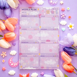 May include: A lavender weekly planner with a grid design, featuring the text "WEEKLY PLAN" and days of the week. The planner has cloud and rose illustrations. Decorative flowers and embellishments surround the planner.