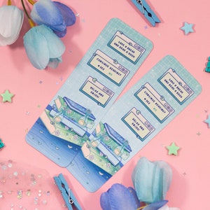 May include: Two blue and green bookmarks with a digital design. The bookmarks feature a stack of books with a moon and stars in the background. The text on the bookmarks reads "Take a break and read a book", "Continue reading?", "Relax and enjoy!"