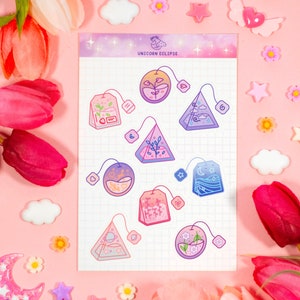 May include: A sheet of stickers featuring nine different tea bag designs. Each tea bag is illustrated with a different nature scene, including a forest, a mountain, a beach, and a starry sky. The stickers are printed on a white background with a grid pattern. The text "UNICORN ECLIPSE" is printed at the top of the sheet.
