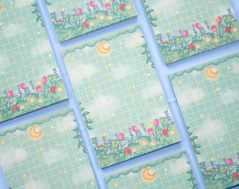 K&ouml;nnte beinhalten: Ein Set aus sechs pastellblauen Notizbl&ouml;cken mit einem Rastermuster und einem floralen Rand. Jeder Notizblock zeigt einen Halbmond und Sterne.