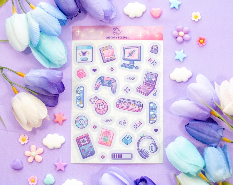 May include: A sheet of stickers featuring a variety of cute, pastel-colored illustrations of video game consoles, controllers, and other gaming-related items. The stickers are arranged in a grid pattern on a white background. The text "Unicorn Eclipse" is printed at the top of the sheet.