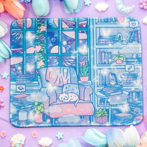 Puede incluir: Un ratón de ordenador azul y blanco con un gato durmiendo en una silla, rodeado de estanterías llenas de libros. El diseño presenta un cielo nocturno estrellado y una ventana con vistas al mar.