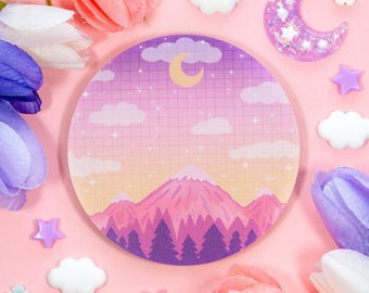 May include: Round notepad with a mountain landscape design. The notepad features a pink and purple gradient sky with a crescent moon, clouds, and stars. The mountains are pink and the trees are purple. The notepad has a grid pattern.