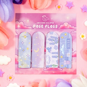 Puede incluir: Un juego de cuatro marcapáginas "Unicorn Eclipse" con diseños pastel. Cada marcapáginas presenta un patrón diferente: estrellas, una luna creciente, ramitas de lavanda y una nube con la hora 11:11. Los marcapáginas están dispuestos sobre un fondo rosa.