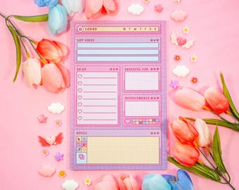 May include: A pink and purple daily planner with sections for "Top 3", "To Do", "Grateful For", "Achievements", and "Notes". The planner has a grid pattern and is decorated with hearts and stars.