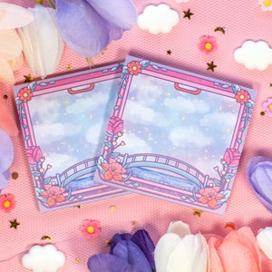 Può includere: Due blocchi di note adesive di colore blu pastello e viola con un design fantasioso che presenta un ponte, nuvole e stelle. I blocchi sono decorati con accenti floreali e sono perfetti per aggiungere un tocco di fantasia a qualsiasi scrivania o planner.
