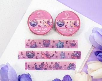 May include: Two rolls of pink washi tape with a Halloween theme. The tape features a cauldron, a ghost, a pumpkin, and a potion bottle. The tape is 15mm wide and 10 meters long. The tape is packaged in a clear plastic container with a pink label that says "Unicorn Eclipse" and "Washi Tape".