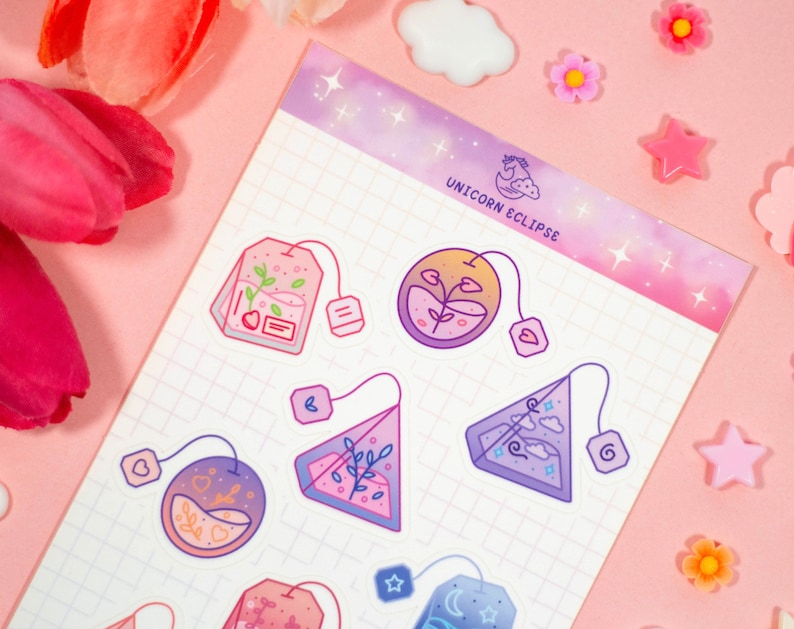 May include: A sheet of stickers featuring various tea bag designs. The stickers are in a variety of colors, including pink, purple, and blue. The stickers are on a pink background with a grid pattern. The text "UNICORN ECLIPSE" is at the top of the sheet.