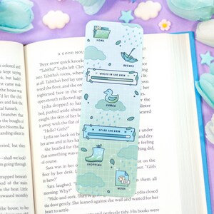 May include: A blue and green bookmark with a whimsical design featuring a duck, rain clouds, and a rain boot. The bookmark has a progress bar with the text "Walks in the Rain" and "After the Rain".