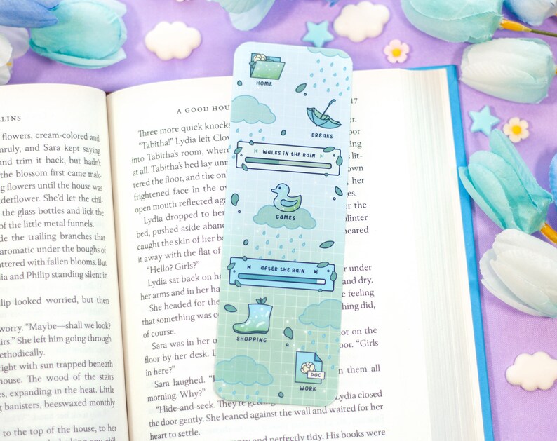 May include: A blue and green bookmark with a whimsical design featuring a duck, rain clouds, and a rain boot. The bookmark has a progress bar with the text "Walks in the Rain" and "After the Rain".