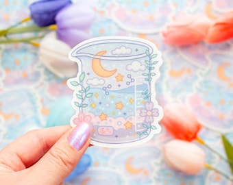 May include: A sticker featuring a beaker design with a whimsical night sky scene. The beaker contains a crescent moon, stars, clouds, and a ladder. The sticker is decorated with floral and vine accents, and is held by a hand with iridescent nail polish.