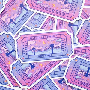May include: A stack of pink and blue ticket-shaped stickers with a design of a night sky with stars, a crescent moon, and a power line with a silhouette of a power pole. The text on the stickers reads "Believe in Yourself" and "Admit One".