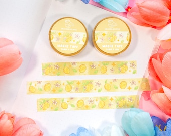 May include: Two rolls of yellow washi tape with a lemon and star design. The tape is on a white surface with pink and blue flowers.