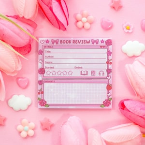 May include: A pink book review notepad with a floral and bow design, surrounded by pink tulips, hearts, stars, and flower-shaped decorations. The notepad includes sections for title, author, genre, and thoughts.