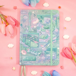 May include: A mint green hardcover journal featuring a collage of musical illustrations including a guitar, keyboard, and record player, with a vertical elastic closure band. The cover displays text that reads "MUSIC TO CHILL UNDER" and "STAY A WHILE AND JUST LISTEN".