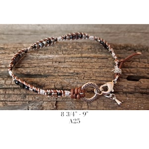 May include: A handcrafted bracelet featuring a braided design with brown leather and silver accents. The bracelet includes black beads and a decorative clasp. The text on the image reads "8 3/4" - 9" A25".