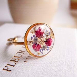 Gold open stainless steel ring with pink-blue bouquet of dried flowers.