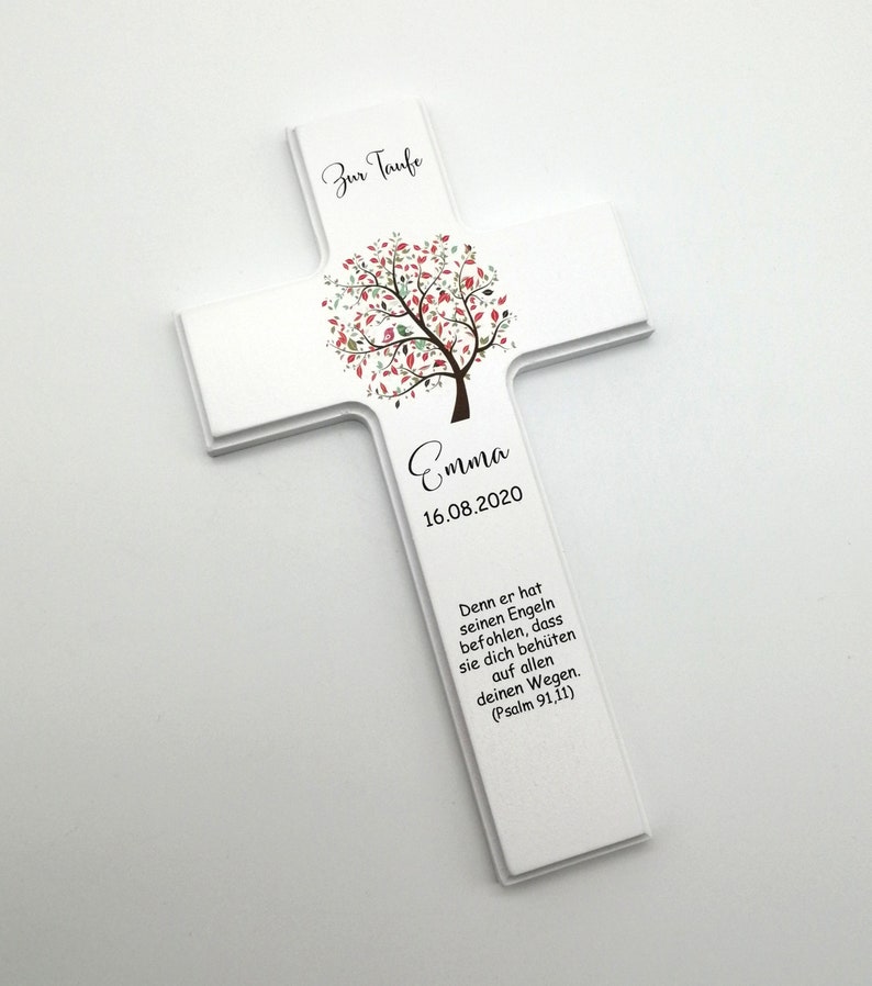 May include: White wooden cross with a stylized tree design in shades of green, pink, and brown. The cross has the text "Zur Taufe" at the top, "Emma" in the center, and "16.08.2020" below the name. The bottom of the cross has a quote in German: "Denn er hat seinen Engeln befohlen, dass sie dich beh&uuml;ten auf allen deinen Wegen. (Psalm 91,11)"