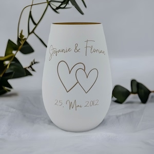 May include: White ceramic vase with a gold rim, featuring two intertwined hearts and the text "Stefanie & Florian 25. Mai 2012".